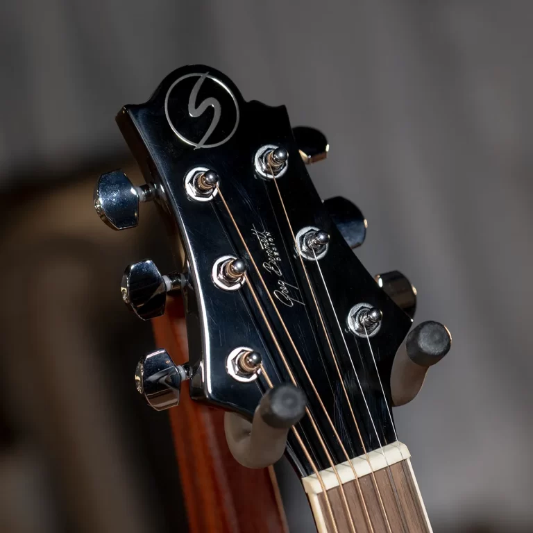 Close-up of a glossy black guitar headstock with six tuning pegs and strings running down the neck, spotlight highlighting the hardware. ขายราคาพิเศษ
