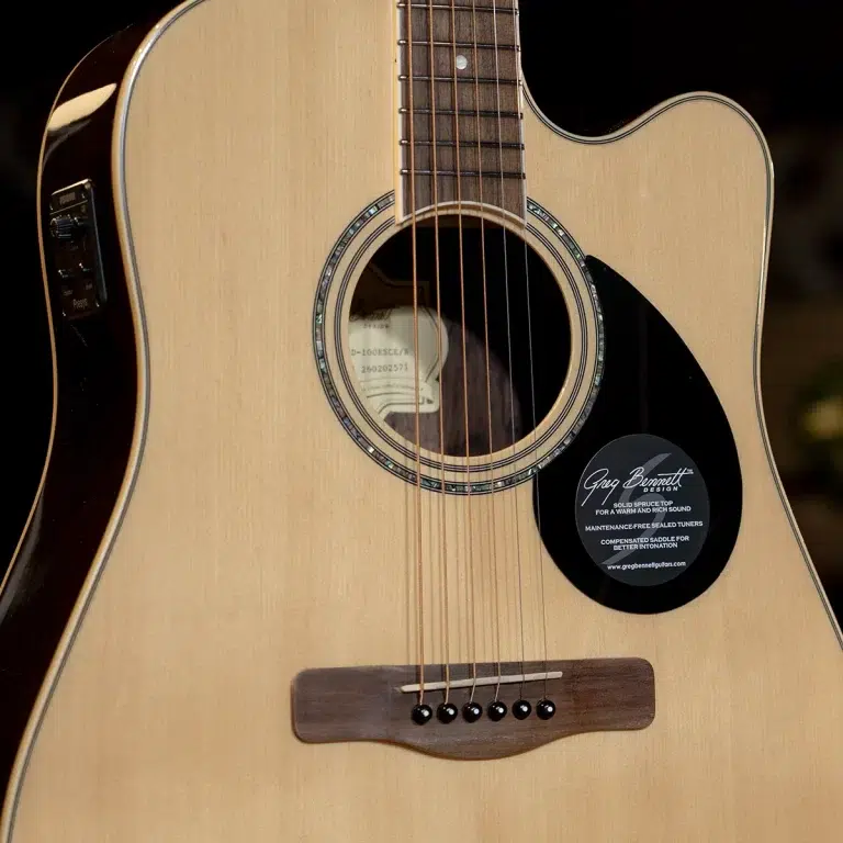 Close-up of an acoustic guitar body showing the soundhole, rosette, six strings, and bridge on a natural wood top, with a black brand sticker near the lower right. ขายราคาพิเศษ