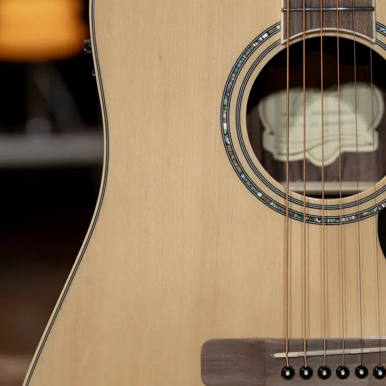 Close-up of an acoustic guitar body showing the soundhole, rosette, and six strings over the bridge with a warm wood finish ขายราคาพิเศษ