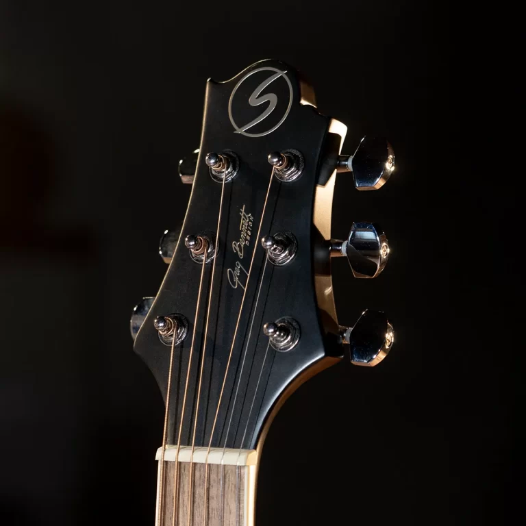 Close-up of a black guitar headstock with six silver tuning pegs and strings against a dark background. ขายราคาพิเศษ