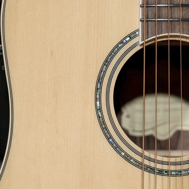 Close-up of an acoustic guitar soundhole with a decorative mother-of-pearl rosette and strings in the foreground. ขายราคาพิเศษ