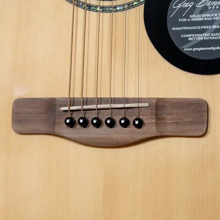 Close-up of a wooden acoustic guitar bridge with six black bridge pins and strings ขายราคาพิเศษ