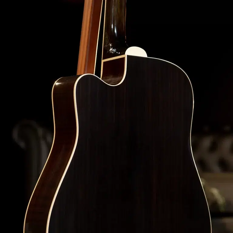 Close-up of the back and side of a dark wooden acoustic guitar, highlighting its curves and cream binding against a black background. ขายราคาพิเศษ