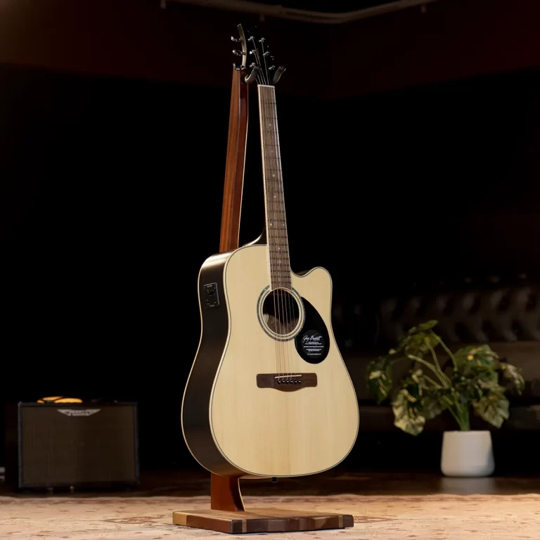 Light-colored acoustic guitar on a wooden stand on a stage, with a small amplifier and potted plant in the background ขายราคาพิเศษ