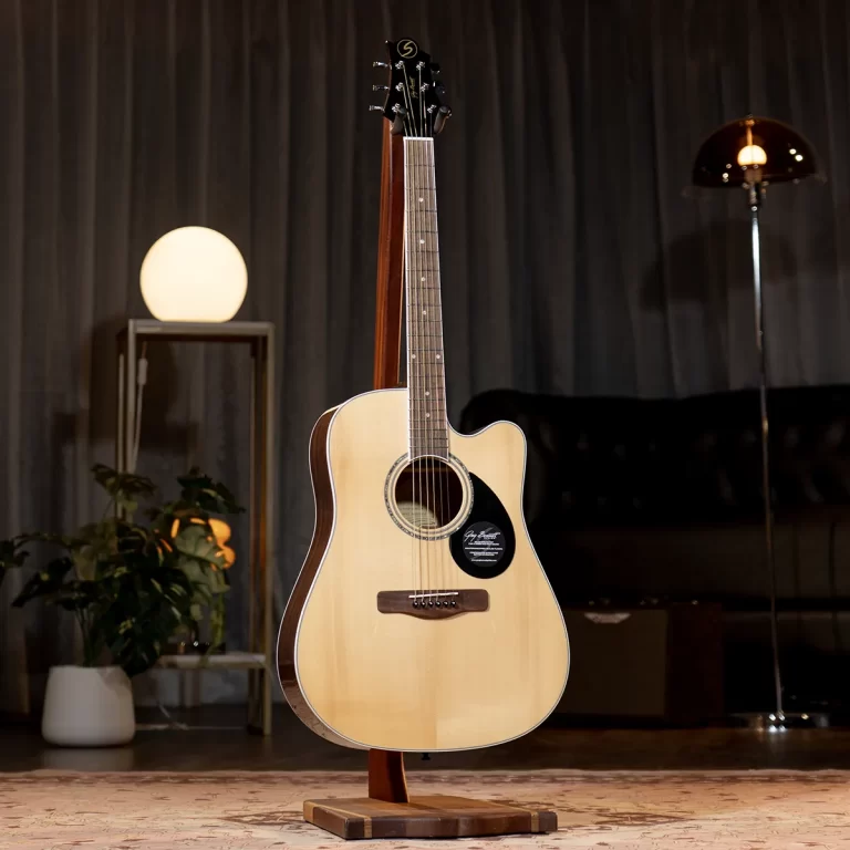 Light-colored acoustic guitar on a stand in a warmly lit room with a planter and lamps. ขายราคาพิเศษ