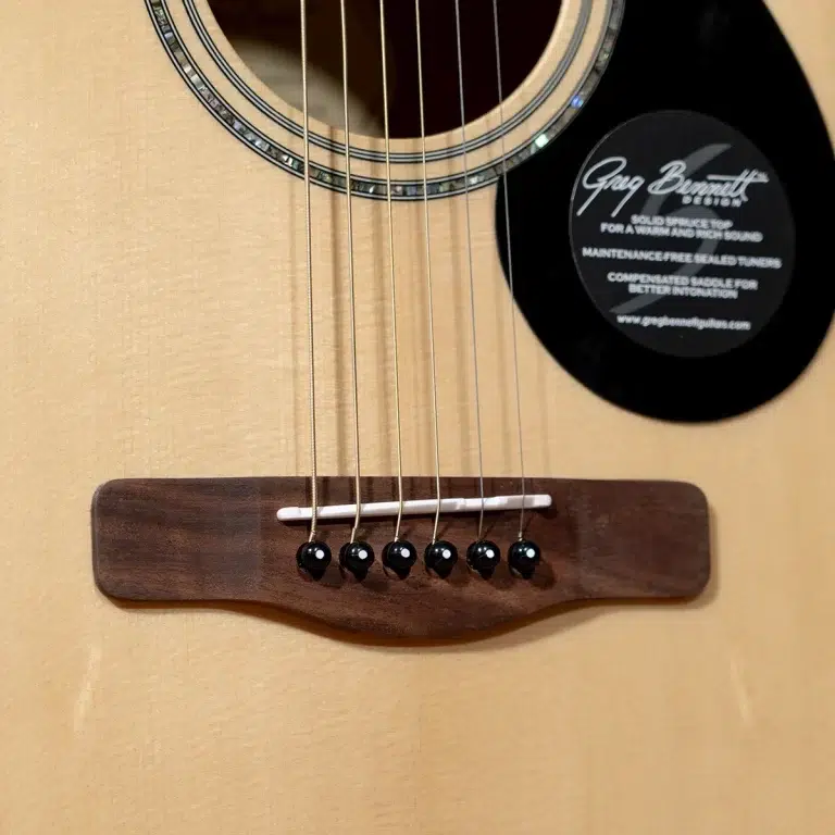 Close-up of an acoustic guitar's bridge and strings on a light wood body, with a black circular label near the soundhole. ขายราคาพิเศษ