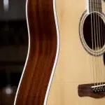 Close-up of an acoustic guitar body: light spruce top with rosette around the sound hole and dark wooden back with white edge binding, showing strings near the bridge. ขายราคาพิเศษ