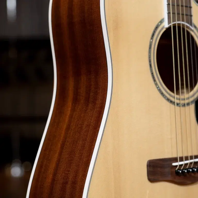Close-up of an acoustic guitar body: light spruce top with rosette around the sound hole and dark wooden back with white edge binding, showing strings near the bridge. ขายราคาพิเศษ