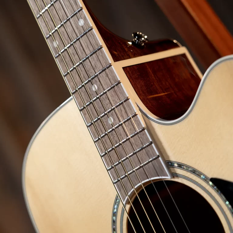 Close-up of an acoustic guitar neck and fretboard with strings and dots, showing the body edge and soundhole rim behind it. ขายราคาพิเศษ