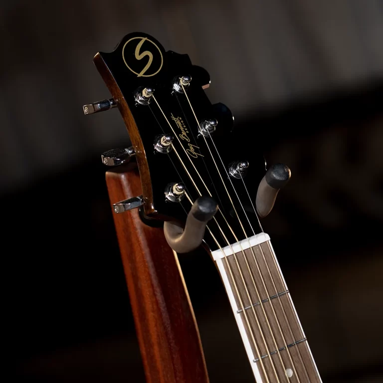 Close-up of a black guitar headstock with six chrome tuners and gold logo visible against a dark background. ขายราคาพิเศษ