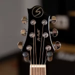 Close-up of a black guitar headstock with six chrome tuning pegs and copper strings, showing the Gibson script logo. ขายราคาพิเศษ