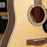 Close-up of an acoustic guitar with a light wood top, circular soundhole, and six strings over the bridge. ขายราคาพิเศษ