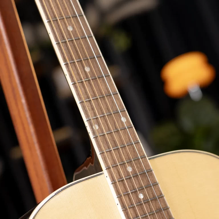 Close-up of an acoustic guitar neck and fretboard with strings and nut visible against a blurred background. ขายราคาพิเศษ