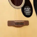 Close-up of an acoustic guitar bridge with six strings and a white saddle on a light wood body, soundhole and label visible. ขายราคาพิเศษ