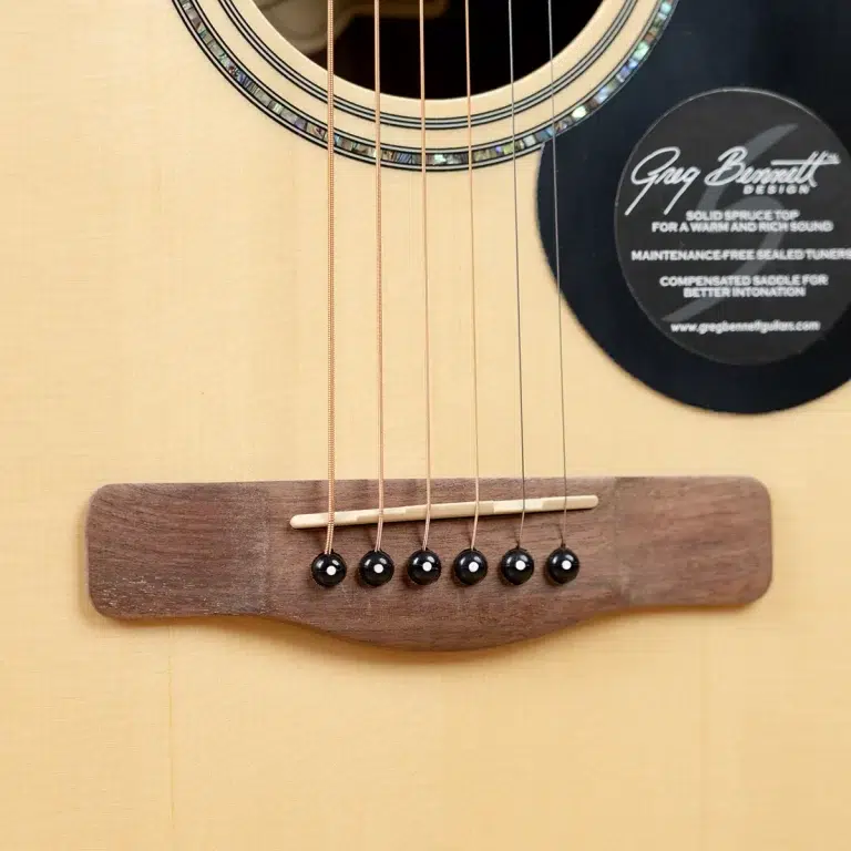 Close-up of an acoustic guitar's bridge, six strings, and saddle on a wooden body. A circular rosette surrounds the soundhole with a label on the right side. ขายราคาพิเศษ