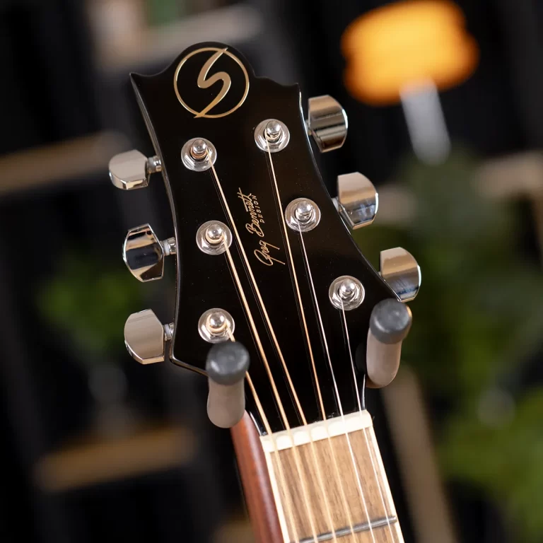 Close-up of a guitar headstock with six chrome tuning pegs and gold strings, logo at the top, and a blurred background. ขายราคาพิเศษ