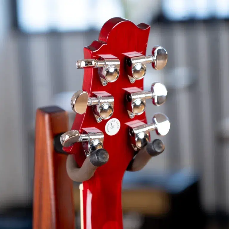 Close-up of a red guitar headstock with chrome tuners and black nut, held in a stand in a blurred background. ขายราคาพิเศษ
