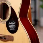 Close-up of an acoustic guitar showing the soundhole, light wood top, tortoiseshell pickguard, and red side/back detail. ขายราคาพิเศษ