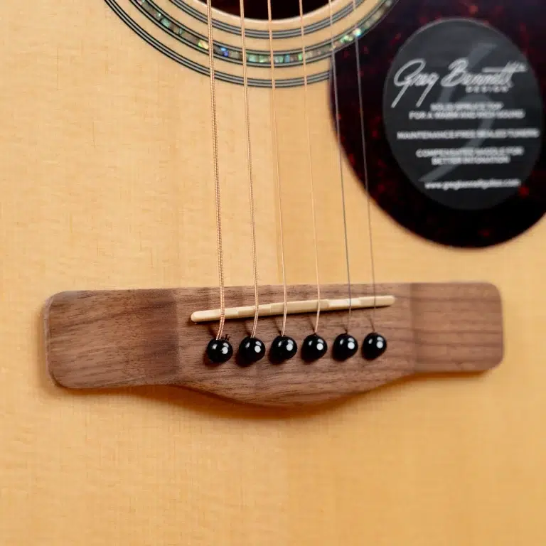 Close-up of an acoustic guitar bridge with six black bridge pins and a saddle wire, on a light wood body surface ขายราคาพิเศษ