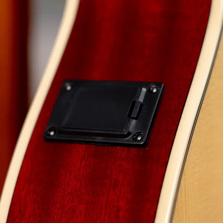 Close-up of the back of a red electric guitar, showing a black rectangular control/battery cover held by four screws with cream binding around the edge. ขายราคาพิเศษ