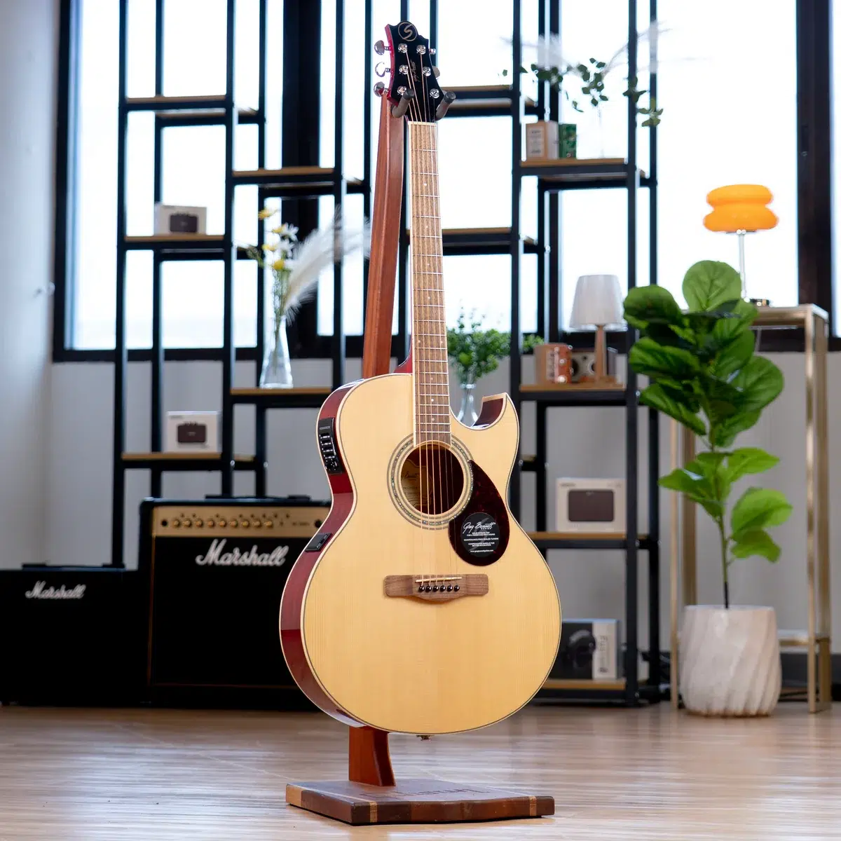 Acoustic guitar on a wooden stand in a modern music shop with amps and shelves in the background