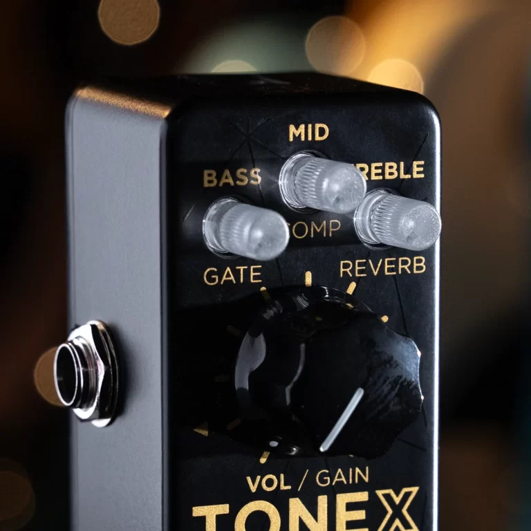 Close-up of a black guitar effects pedal with gold labels for BASS, MID, TREBLE, COMP, GATE, and REVERB; several knobs and a large dial in focus against a blurred background. ขายราคาพิเศษ