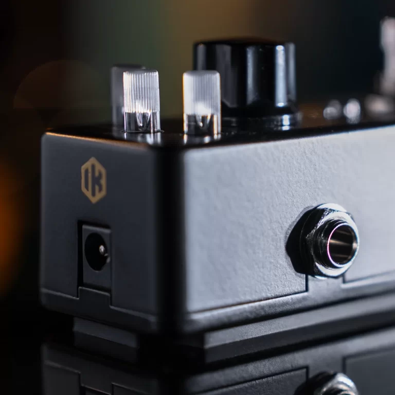 Close-up of a guitar effects pedal side with input jack, power port, and two clear knobs; brand logo visible on the black chassis. ขายราคาพิเศษ