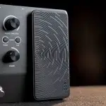 Close-up of a black audio speaker with a textured circular grill, standing beside a control panel with knobs and labels like SELECT/MASTER and HOME. ขายราคาพิเศษ