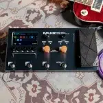 Black guitar multi-effects pedal with a small color LCD, orange knobs, and four footswitches labeled A, B, C, CTRL, on a patterned rug with a red guitar nearby. ขายราคาพิเศษ