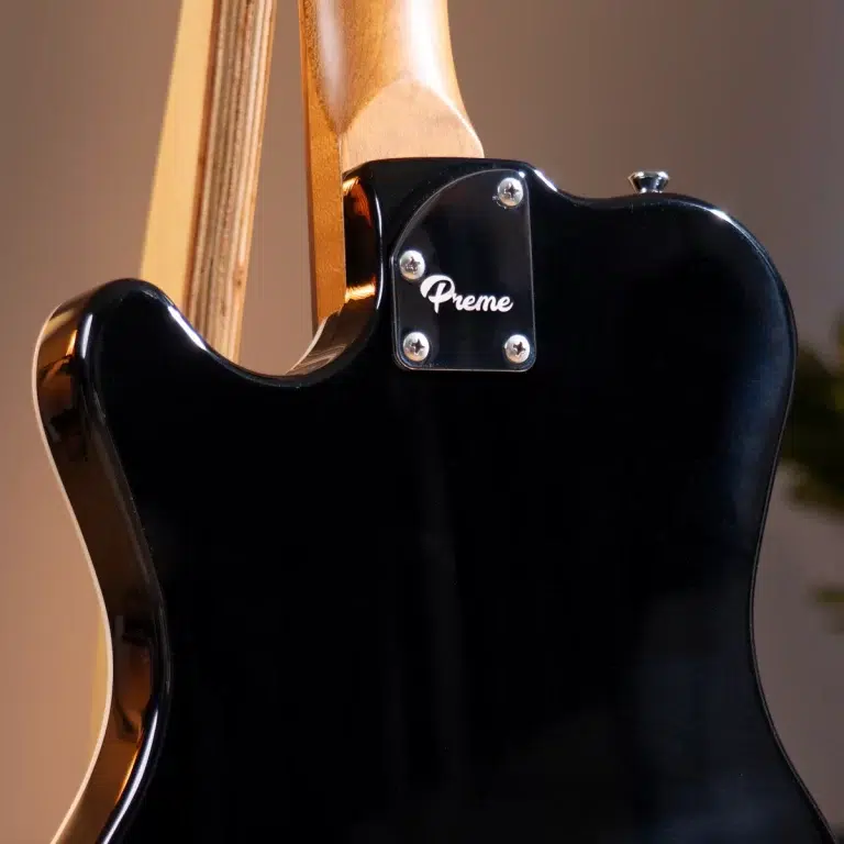 Close-up of the back of a glossy black electric guitar with a chrome neck plate showing the word 'Preme' and four screws, wood neck visible ขายราคาพิเศษ