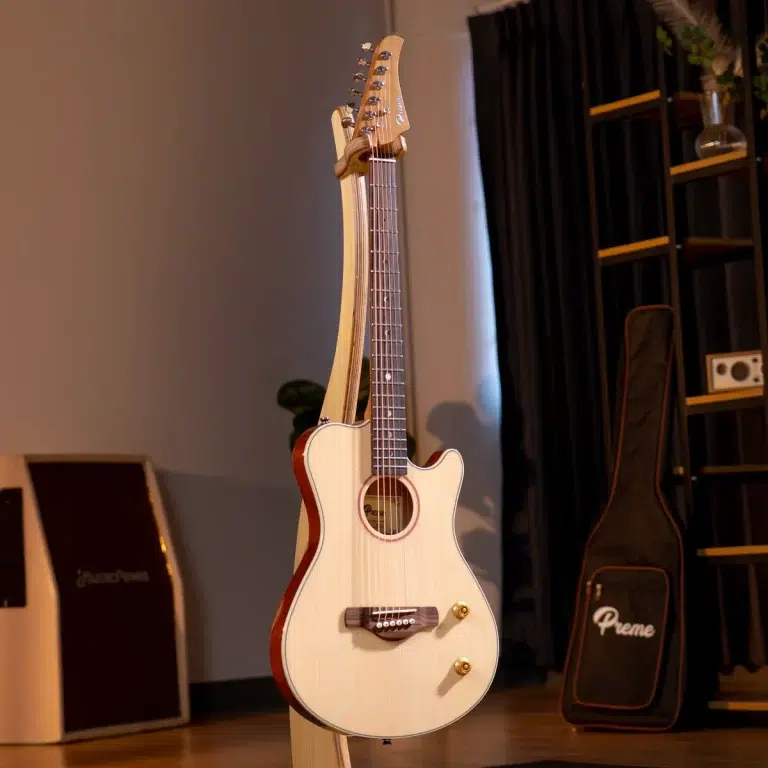 Cream-colored acoustic guitar with a cutaway on a wooden stand, in a dim room with shelves and gear cases nearby. ขายราคาพิเศษ