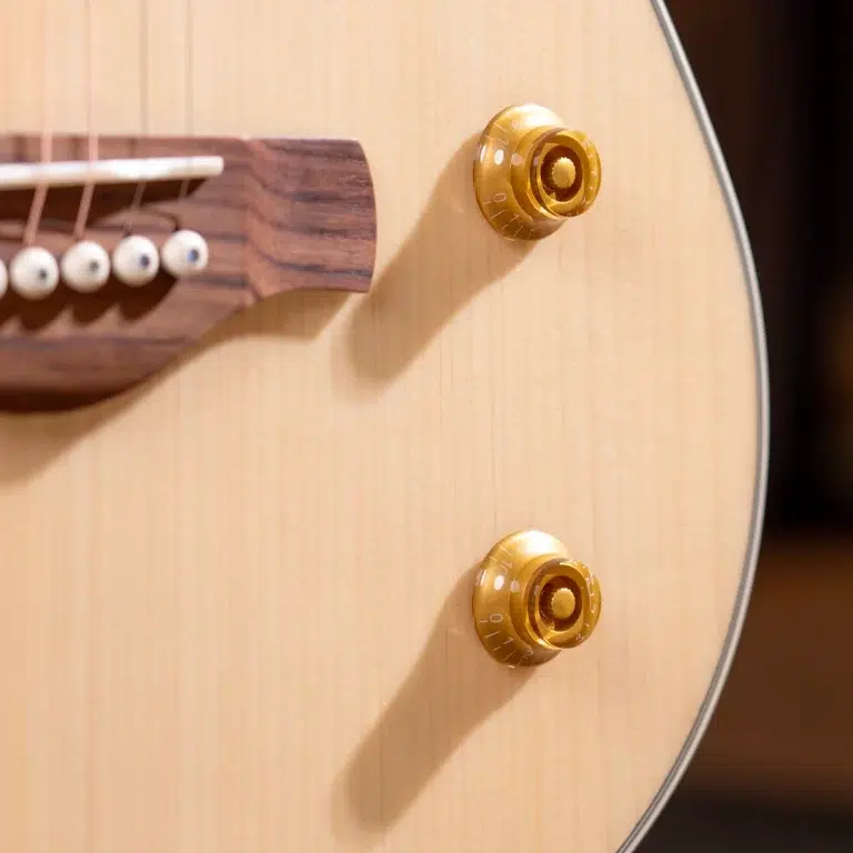 Close-up of a light wood acoustic guitar body showing two gold control knobs and part of the bridge saddles with strings nearby. ขายราคาพิเศษ