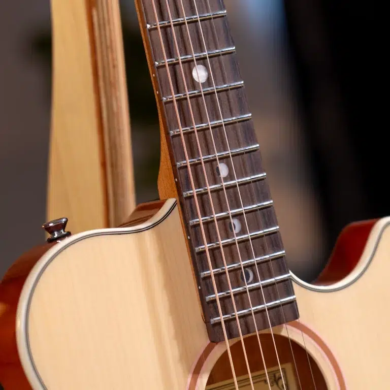 Close-up of an acoustic guitar neck with metal frets and six strings along a wooden fretboard ขายราคาพิเศษ