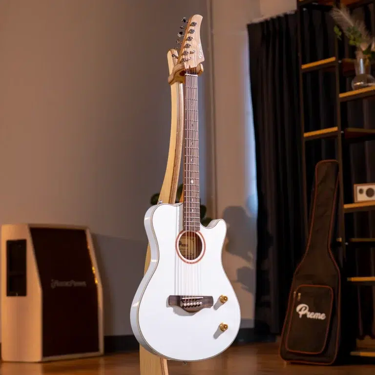 White cutaway acoustic-electric guitar on a stand in a music studio, with amps and a guitar case visible in the background. ขายราคาพิเศษ