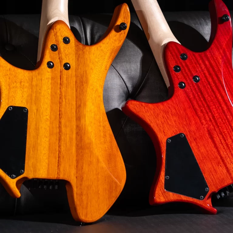 Two electric guitars with natural orange and red wood finishes leaning against a dark surface, showing black back plates and hardware. ขายราคาพิเศษ