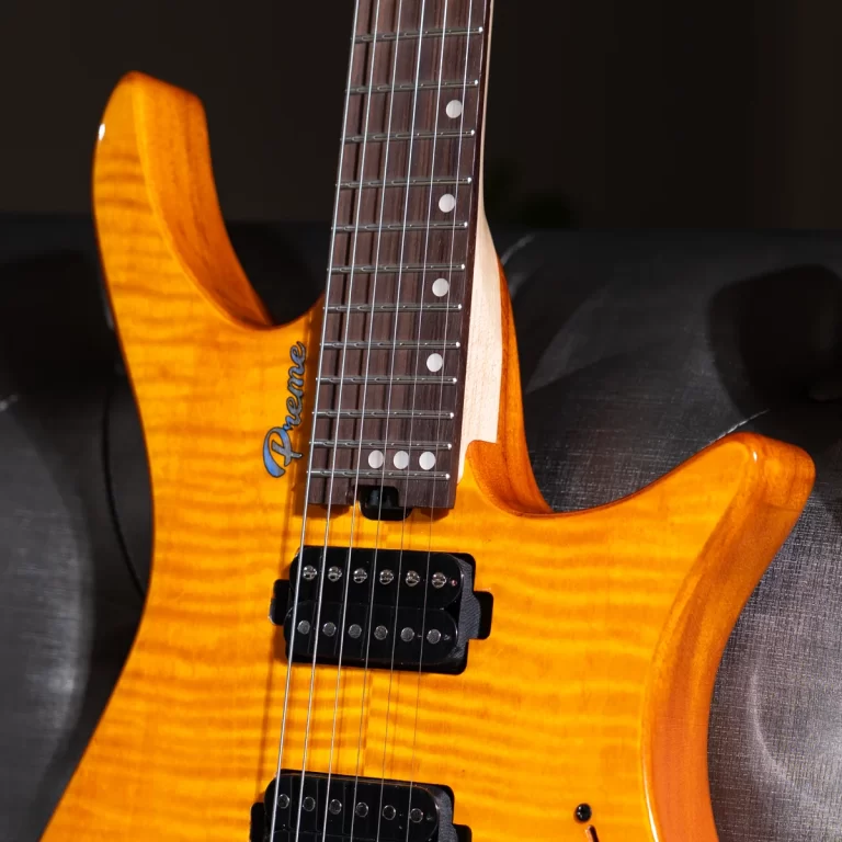 Close-up of an orange electric guitar with a quilted maple top, showing the neck, frets, and black pickups on a dark sofa. ขายราคาพิเศษ