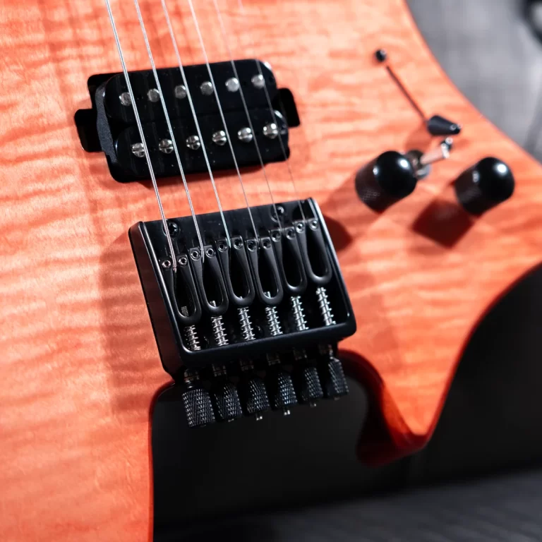 Close-up of an orange electric guitar body showing a black tremolo bridge and pickups with six strings ribbing across the fretboard area on a dark background ขายราคาพิเศษ
