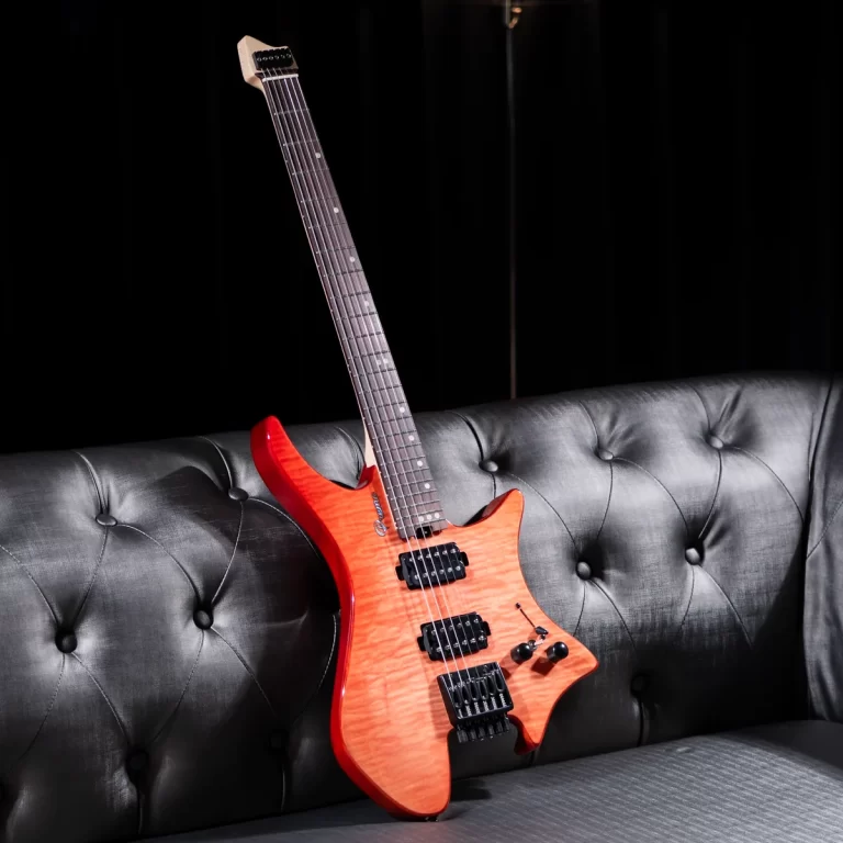Orange electric guitar with a quilted top, two humbucker pickups, and a black tremolo bridge, leaning on a tufted gray sofa against a black backdrop. ขายราคาพิเศษ