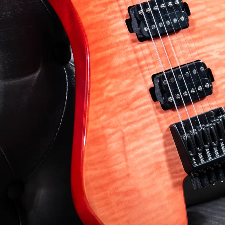 Close-up of a red-orange electric guitar body showing two black humbucker pickups and a chrome bridge with strings, wood grain finish visible. ขายราคาพิเศษ