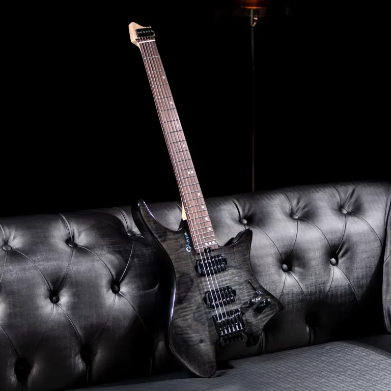 Black electric guitar with a light brown neck leaning on a tufted gray leather sofa in a dark studio setting. ขายราคาพิเศษ