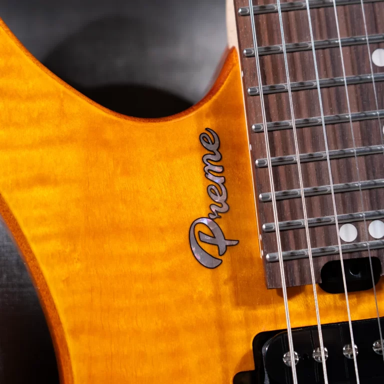 Close-up of an orange electric guitar body with a black script logo along the edge and part of the fretboard and strings visible. ขายราคาพิเศษ