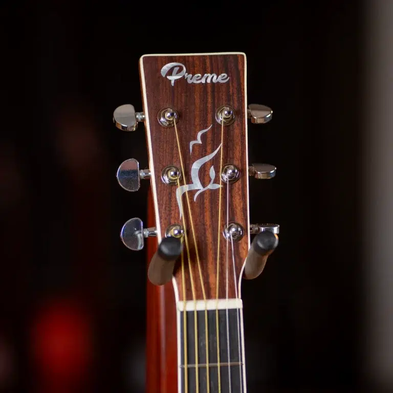 Woodgrain guitar headstock with six tuning pegs and a white 'Preme' logo, strings visible over the nut against a dark background ขายราคาพิเศษ