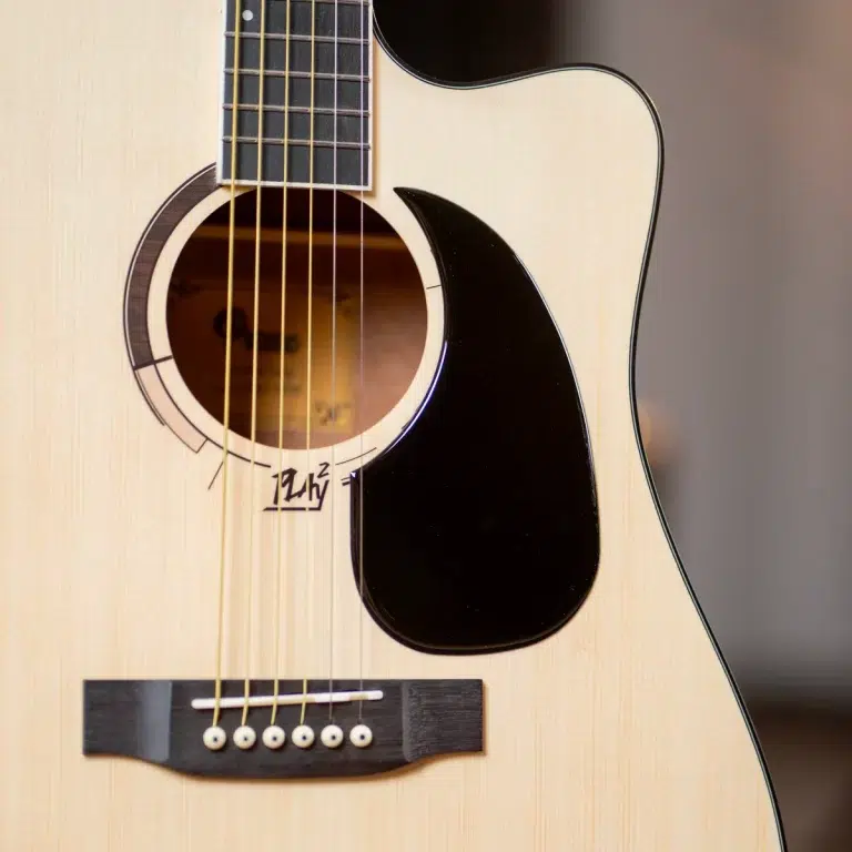 Close-up of a light-colored acoustic guitar showing the soundhole, strings, and black pickguard on the body. ขายราคาพิเศษ