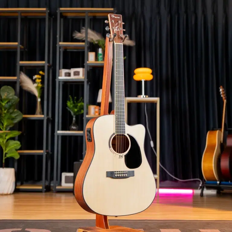 Acoustic guitar on a wooden stand in a music studio, with shelves and a second guitar in the background. ขายราคาพิเศษ