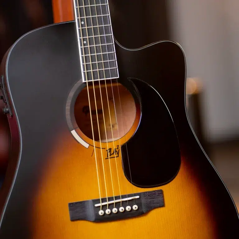 Sunburst acoustic guitar close-up showing soundhole, fretboard, and black pickguard with six strings. ขายราคาพิเศษ