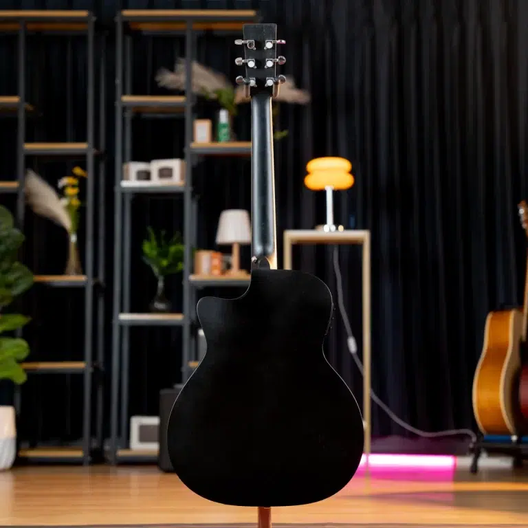 Black semi-hollow body guitar on a stand facing away, on a stage with shelving and warm lighting in the background. ขายราคาพิเศษ