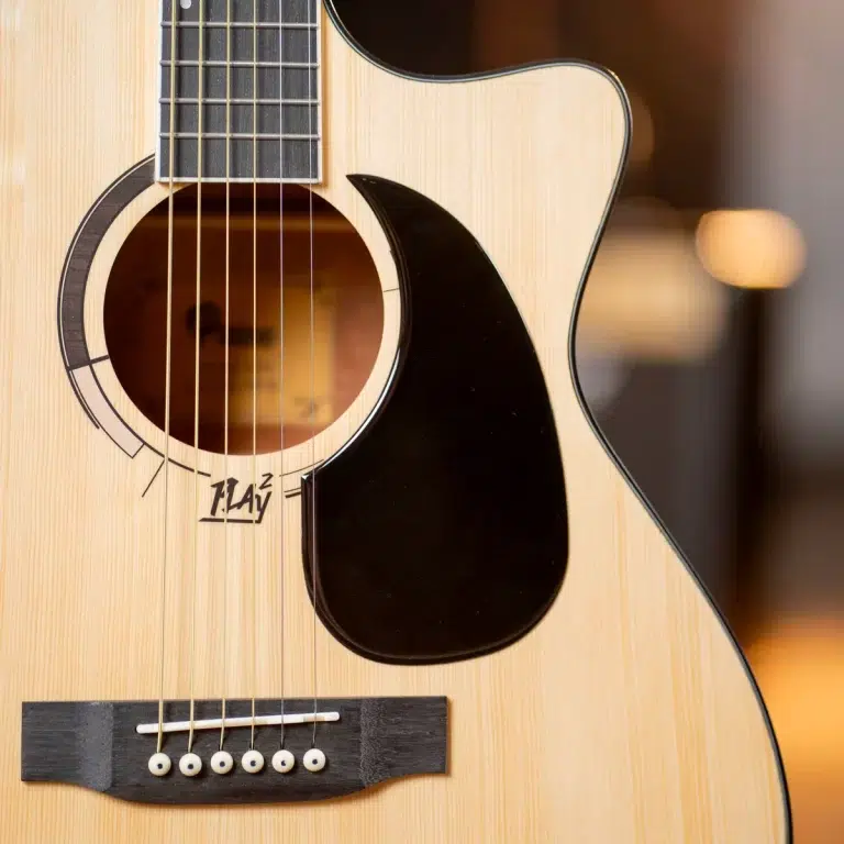 Close-up of an acoustic guitar showing a natural wood body, round sound hole, black pickguard, and six strings over the bridge. ขายราคาพิเศษ