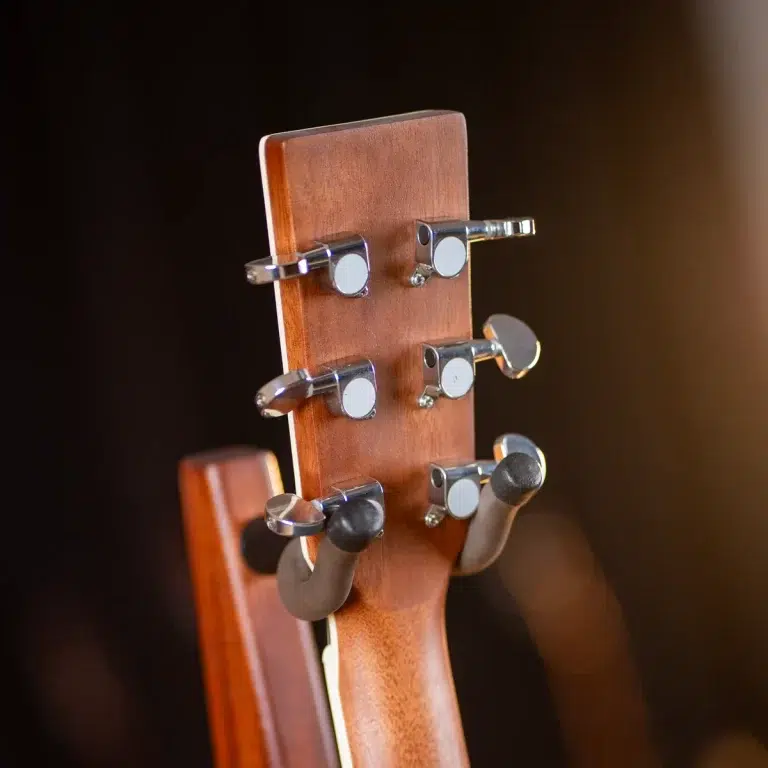 Close-up of a wooden guitar headstock with six chrome tuning pegs and string posts visible on a dark background. ขายราคาพิเศษ