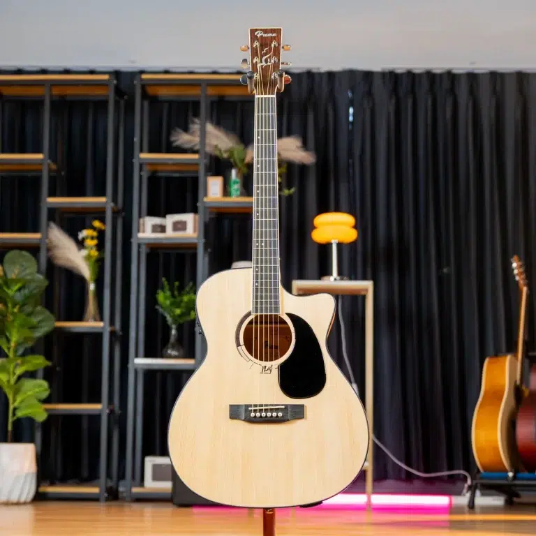 Acoustic guitar on a stand in a studio showroom with black curtains and shelving in the background. ขายราคาพิเศษ