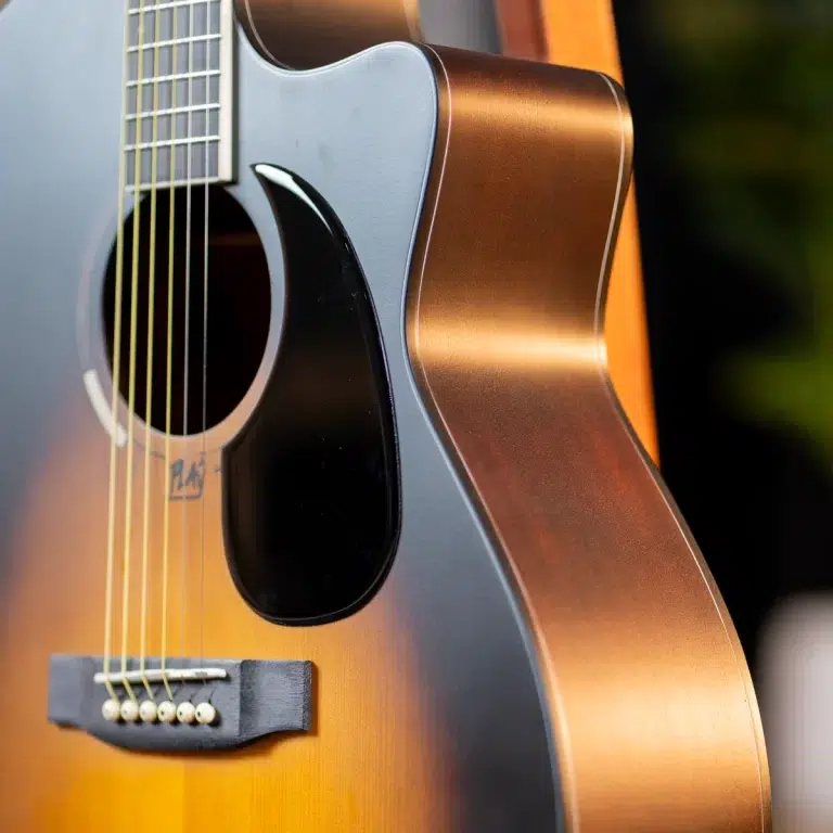 Close-up of an acoustic guitar's sunburst body, strings, bridge, and black pickguard around the soundhole. ขายราคาพิเศษ